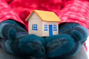 person with mittens holding a mini house